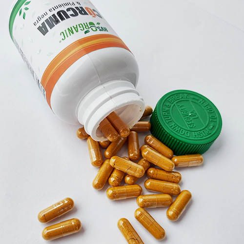 Cápsulas de cúrcuma HVS Organic saliendo del frasco, detalle en primer plano